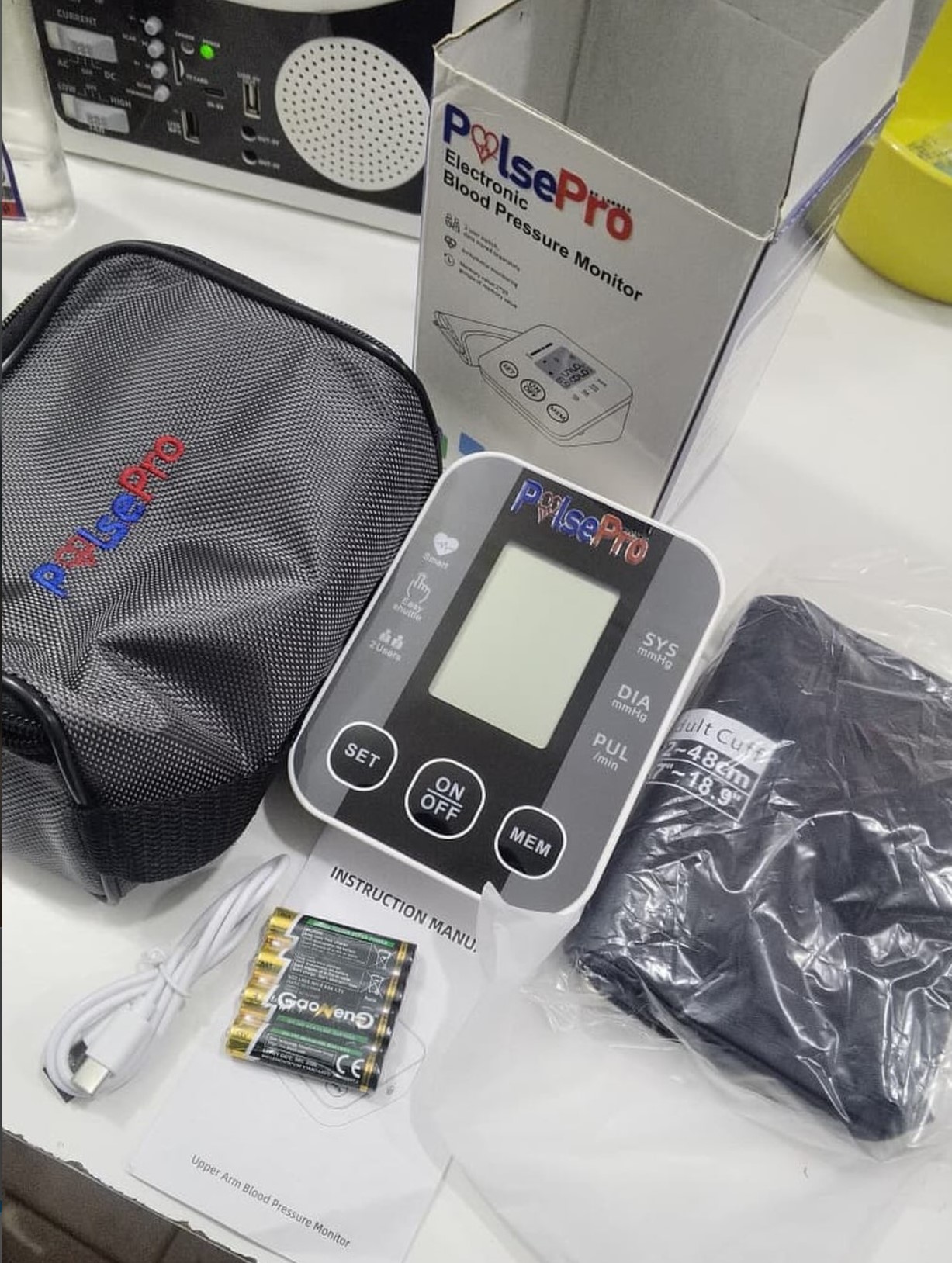 PulsePro upper-arm digital blood pressure monitor with cuff, batteries, carry case and manual on a white studio background